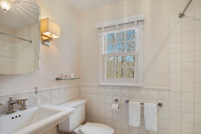 full bathroom with toilet, tiled shower, tile walls, and a sink