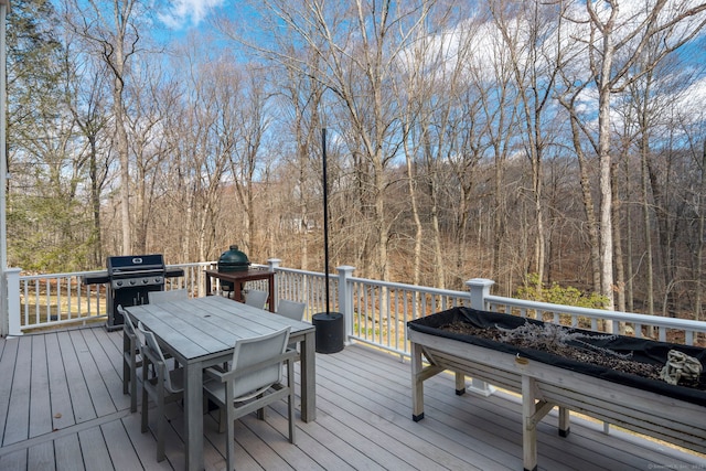 wooden terrace featuring outdoor dining area, a view of trees, and a grill