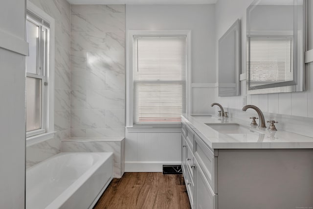 full bathroom featuring a sink, a bathing tub, wood finished floors, wainscoting, and double vanity