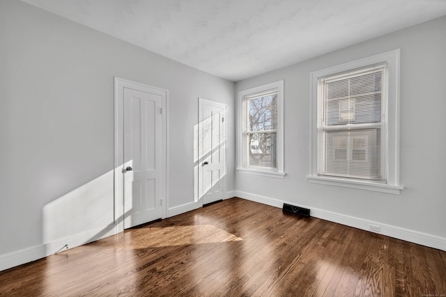 empty room with visible vents, dark wood-type flooring, and baseboards