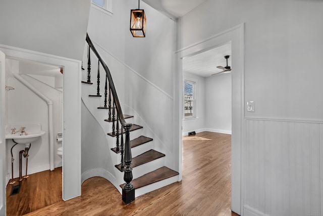 staircase with a wainscoted wall, wood finished floors, and a ceiling fan