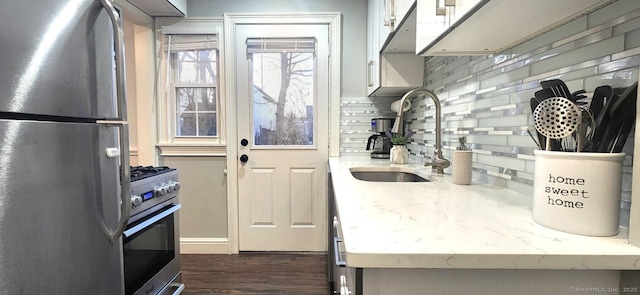 kitchen with light stone counters, dark wood finished floors, a sink, decorative backsplash, and appliances with stainless steel finishes