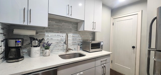 kitchen featuring light stone countertops, a toaster, white cabinets, fridge, and a sink