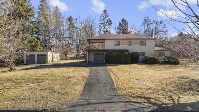 traditional-style house featuring a front lawn, an outbuilding, a garage, and aphalt driveway