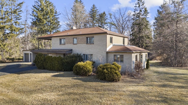 rear view of property featuring brick siding, a lawn, a chimney, and a garage