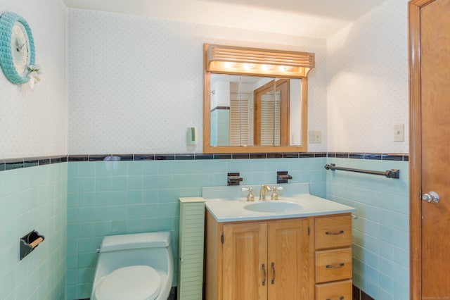 bathroom with a wainscoted wall, toilet, vanity, and wallpapered walls