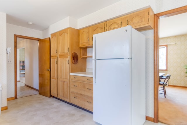 kitchen with wallpapered walls, baseboards, light countertops, light carpet, and freestanding refrigerator