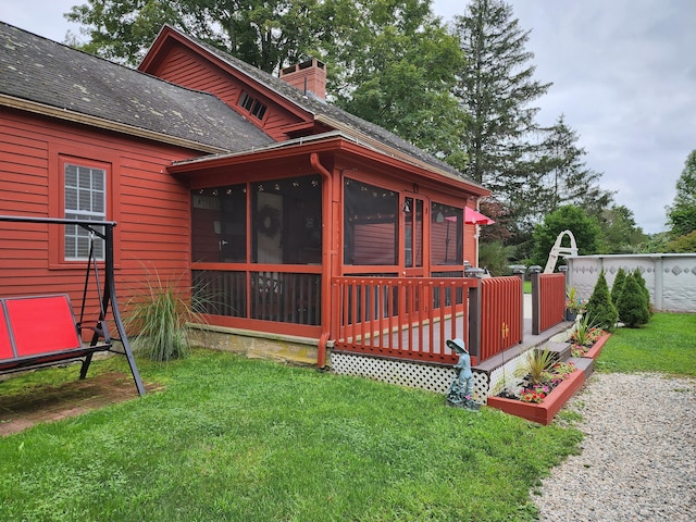 back of house with a shingled roof, a sunroom, a chimney, a deck, and a yard