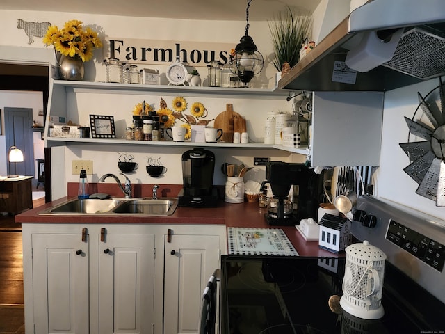 kitchen with a sink, open shelves, dark countertops, wood finished floors, and wall chimney exhaust hood