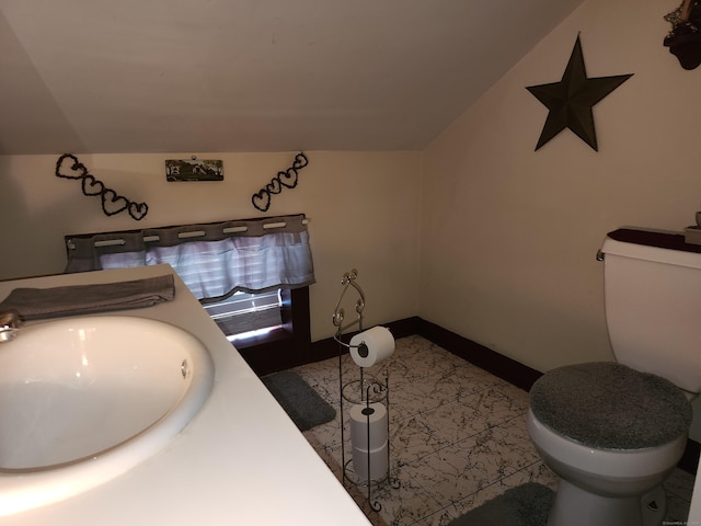 bathroom featuring vaulted ceiling, toilet, baseboards, and a sink