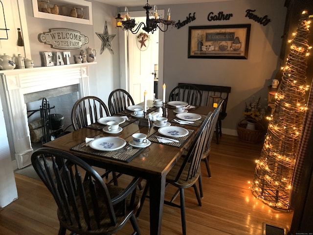 dining area featuring wood finished floors, baseboards, visible vents, a fireplace, and a chandelier