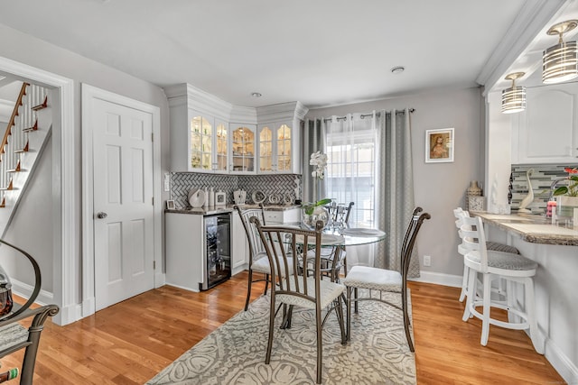 dining room featuring bar area, baseboards, beverage cooler, stairway, and light wood-type flooring