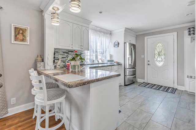 kitchen with backsplash, a breakfast bar, a peninsula, stainless steel refrigerator with ice dispenser, and white cabinetry