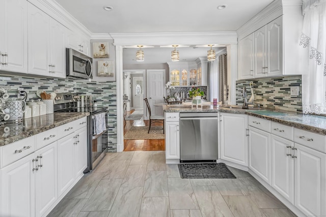 kitchen featuring backsplash, ornamental molding, appliances with stainless steel finishes, white cabinetry, and a sink