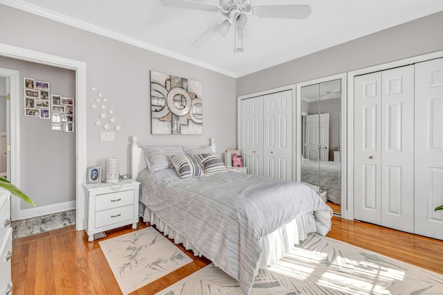 bedroom featuring a ceiling fan, baseboards, light wood-style flooring, ornamental molding, and multiple closets