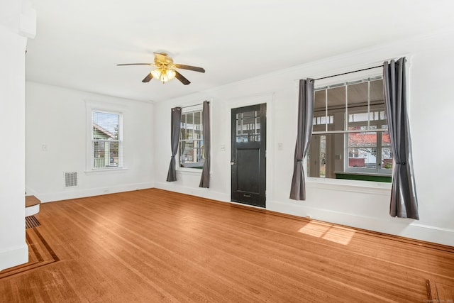 empty room featuring a ceiling fan, wood finished floors, visible vents, and baseboards