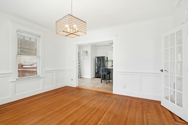 empty room featuring a notable chandelier, wood finished floors, crown molding, and a decorative wall