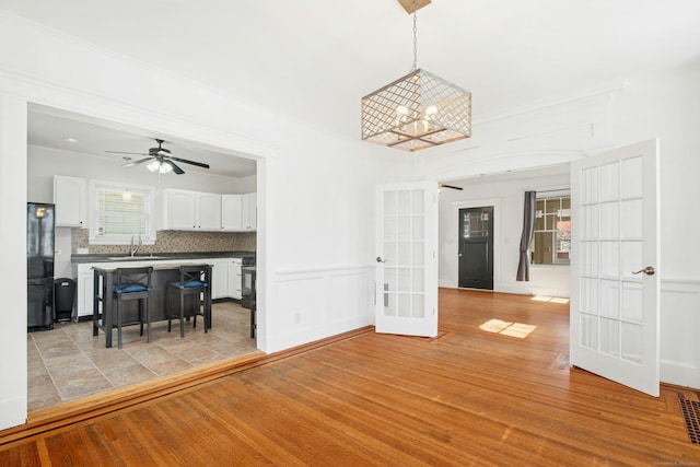 living area with french doors, light wood-style floors, crown molding, and ceiling fan with notable chandelier