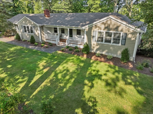 view of front of property featuring a chimney, roof with shingles, covered porch, and a front lawn