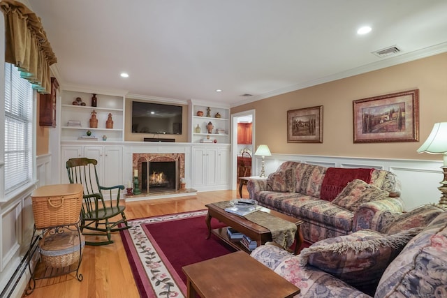 living room featuring a premium fireplace, visible vents, light wood-style flooring, and ornamental molding