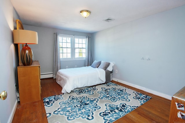 bedroom with wood finished floors, visible vents, baseboard heating, and baseboards