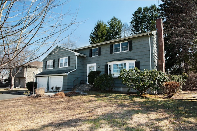 colonial-style house featuring aphalt driveway, a garage, and a chimney