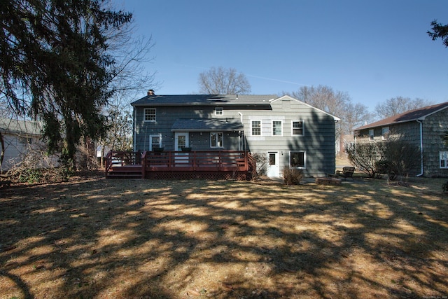 back of property featuring a deck, a chimney, and a yard