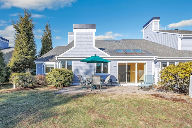 rear view of house with a shingled roof, roof mounted solar panels, a chimney, a yard, and a patio area