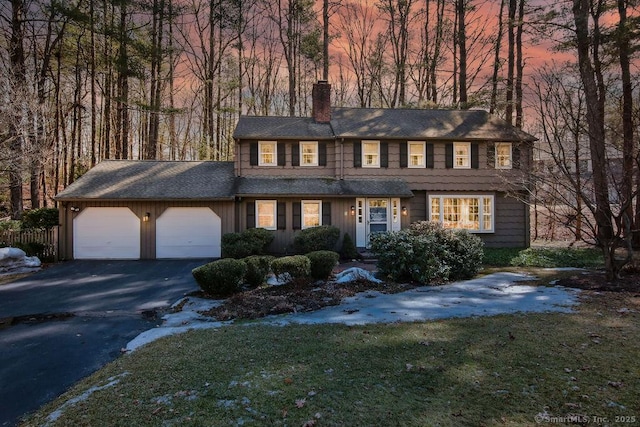 view of front facade featuring a garage, a front yard, a chimney, and aphalt driveway