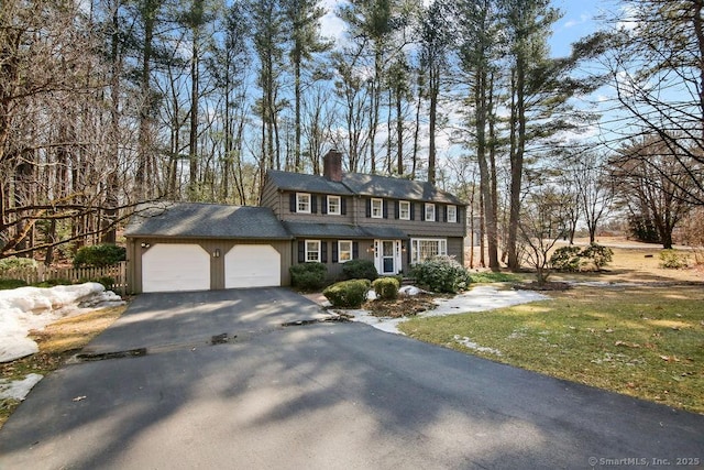 colonial-style house with aphalt driveway, fence, a garage, and a chimney