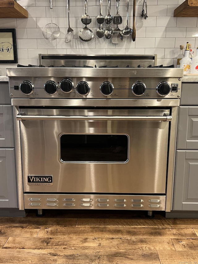 room details with backsplash, wood finished floors, gray cabinets, and designer range