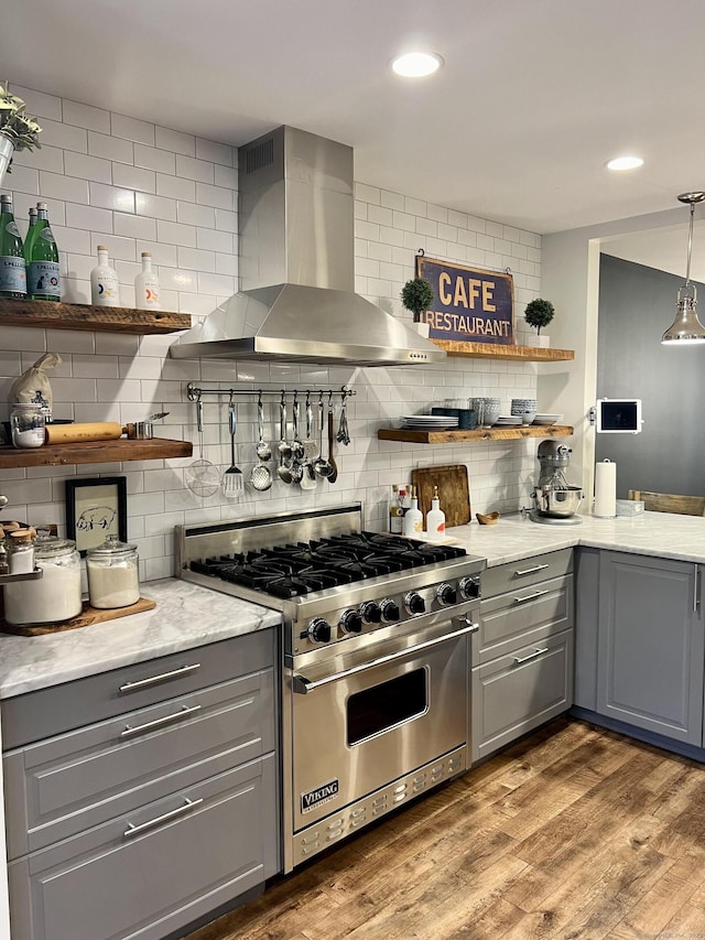 kitchen with wood finished floors, open shelves, luxury stove, gray cabinetry, and wall chimney range hood