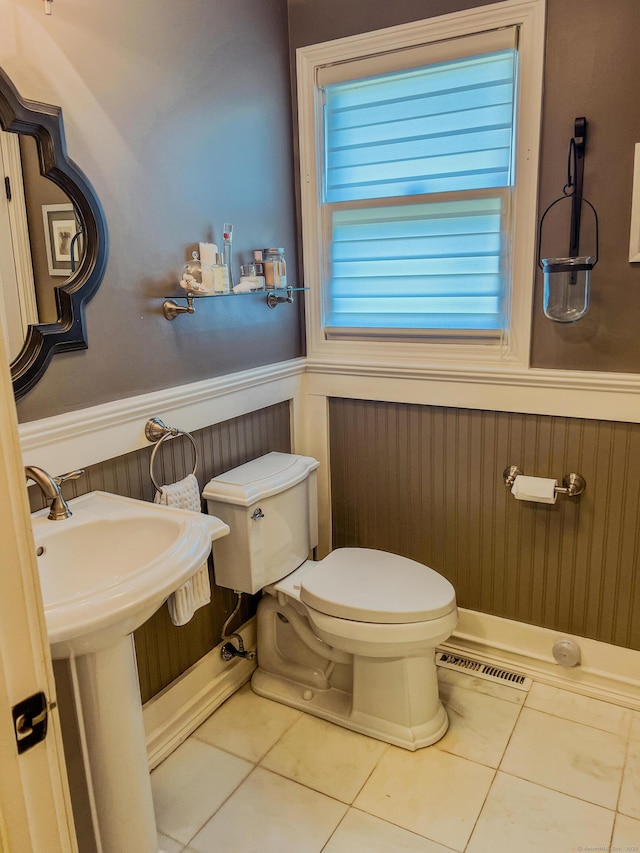 half bathroom with visible vents, toilet, a sink, wainscoting, and tile patterned flooring