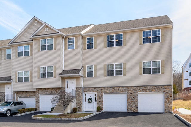 view of front of house featuring aphalt driveway, stone siding, a garage, and roof with shingles