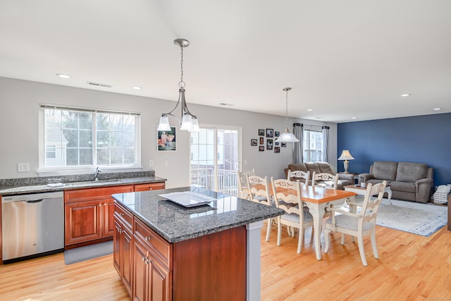 kitchen with light wood-type flooring, visible vents, a sink, a kitchen island, and stainless steel dishwasher