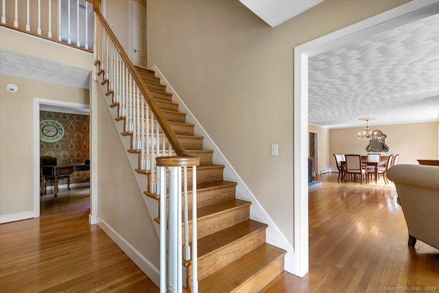 stairs with a notable chandelier, wood finished floors, baseboards, and a textured ceiling