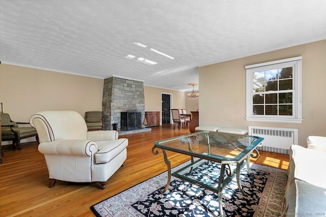 living area with wood finished floors, radiator heating unit, a stone fireplace, a textured ceiling, and a notable chandelier