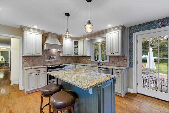 kitchen featuring custom range hood, a sink, decorative light fixtures, stainless steel appliances, and light wood finished floors