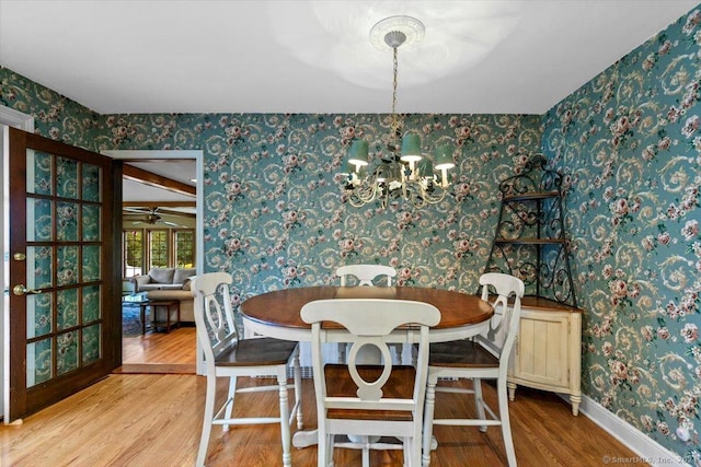 dining area featuring wallpapered walls, ceiling fan with notable chandelier, wood finished floors, and baseboards