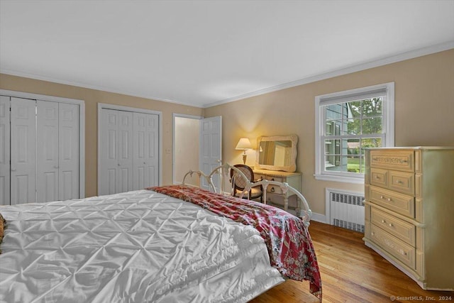 bedroom featuring radiator, wood finished floors, baseboards, ornamental molding, and multiple closets