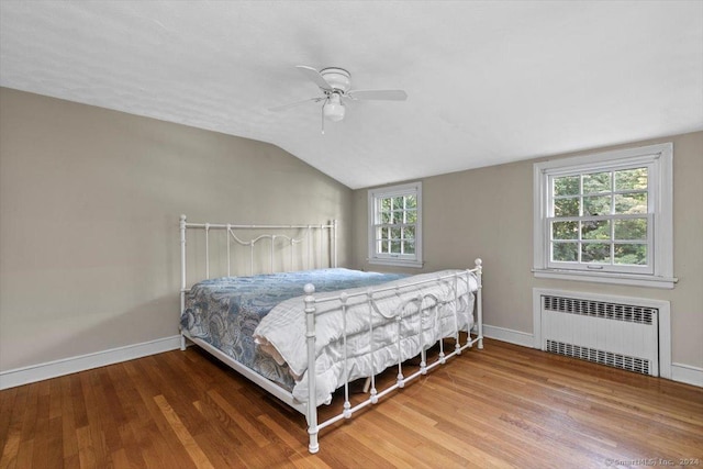 bedroom with lofted ceiling, radiator, wood finished floors, and baseboards