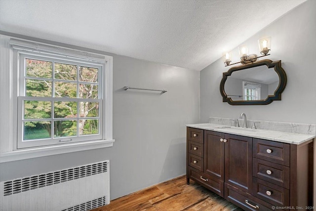 bathroom featuring a textured ceiling, wood finished floors, radiator heating unit, lofted ceiling, and vanity