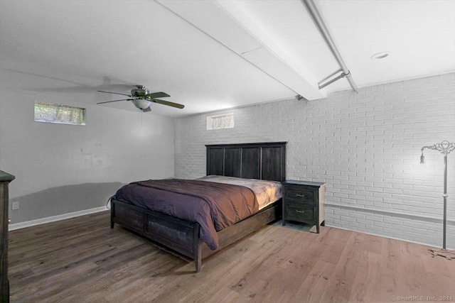 bedroom featuring beamed ceiling, wood finished floors, brick wall, baseboards, and ceiling fan