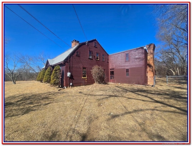 back of house with a gambrel roof, a chimney, and fence