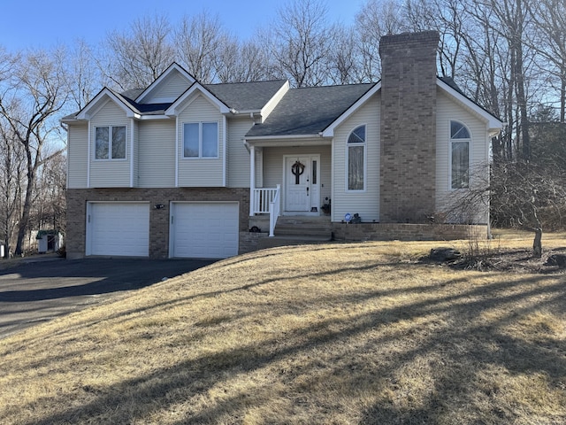 tri-level home with driveway, a chimney, a front lawn, a garage, and brick siding