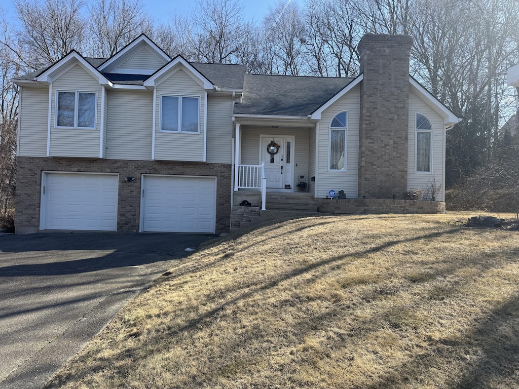 tri-level home featuring brick siding, a shingled roof, aphalt driveway, a chimney, and a garage