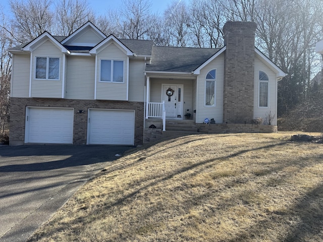 split level home with aphalt driveway, an attached garage, a chimney, and brick siding