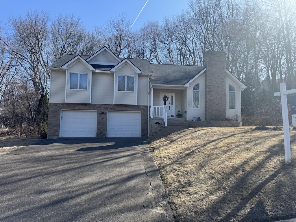 tri-level home featuring aphalt driveway, an attached garage, brick siding, and a chimney