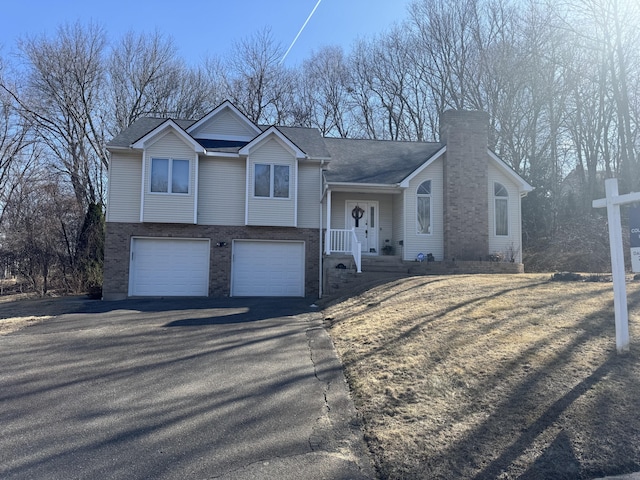 tri-level home featuring aphalt driveway, an attached garage, brick siding, and a chimney