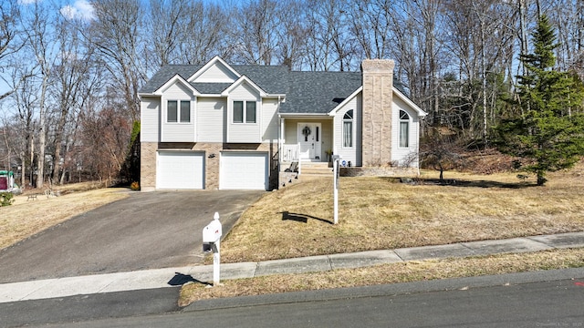 split level home with aphalt driveway, roof with shingles, a front yard, an attached garage, and a chimney